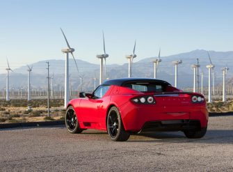 L'arrière d'une Tesla Roadster rouge devant des éoliennes